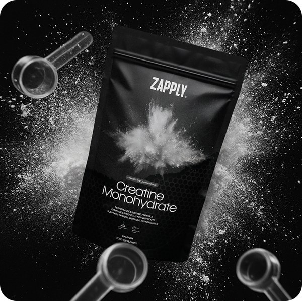 Black Zapply creatine pouch with two measuring scoops and loose white powder on a dark surface