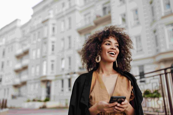 Smiling woman holding her phone on a city street
