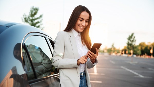 Woman checking her phone next to a rental car in an open car park