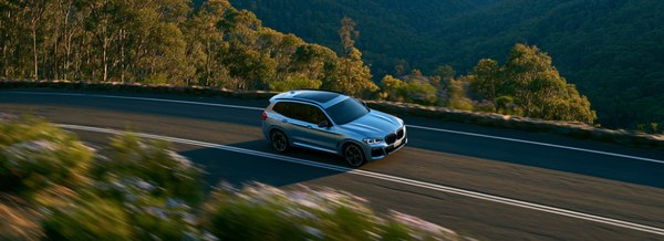 Light blue SUV driving along a winding road through green forest