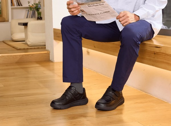 A man seated in black FitVille EasyTop Deluxe dress shoes and navy trousers