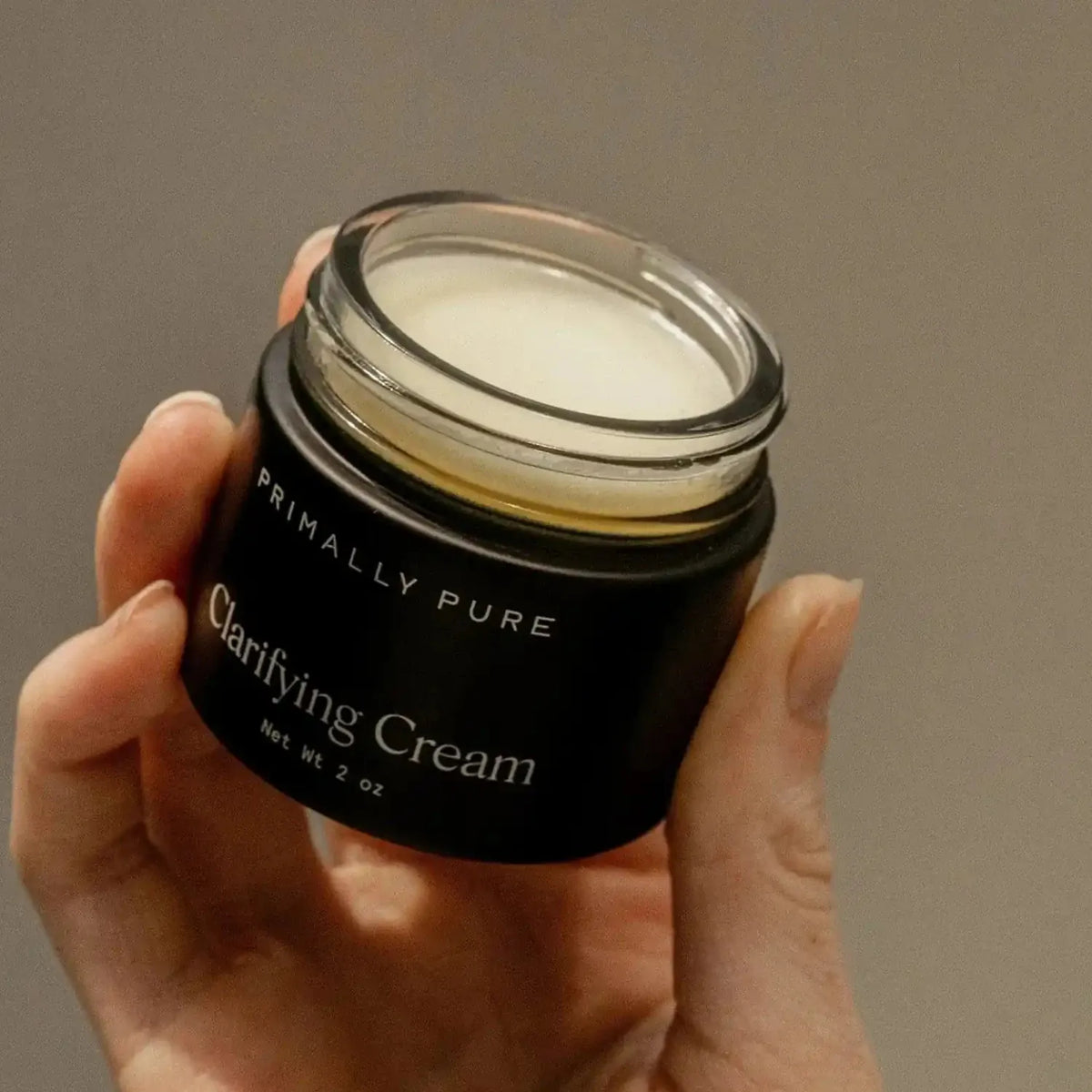Hand holding an open jar of Primally Pure Clarifying Cream