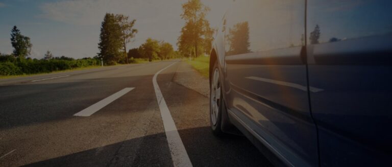 Car driving on an asphalt road at dusk with a close view of the front tyre