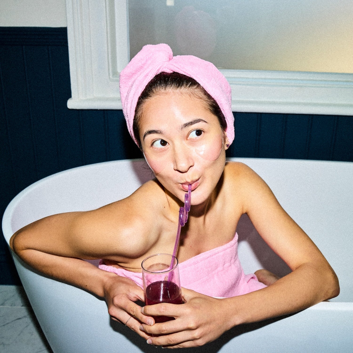 Woman in a bath drinking a pink Glow Dust drink through a straw