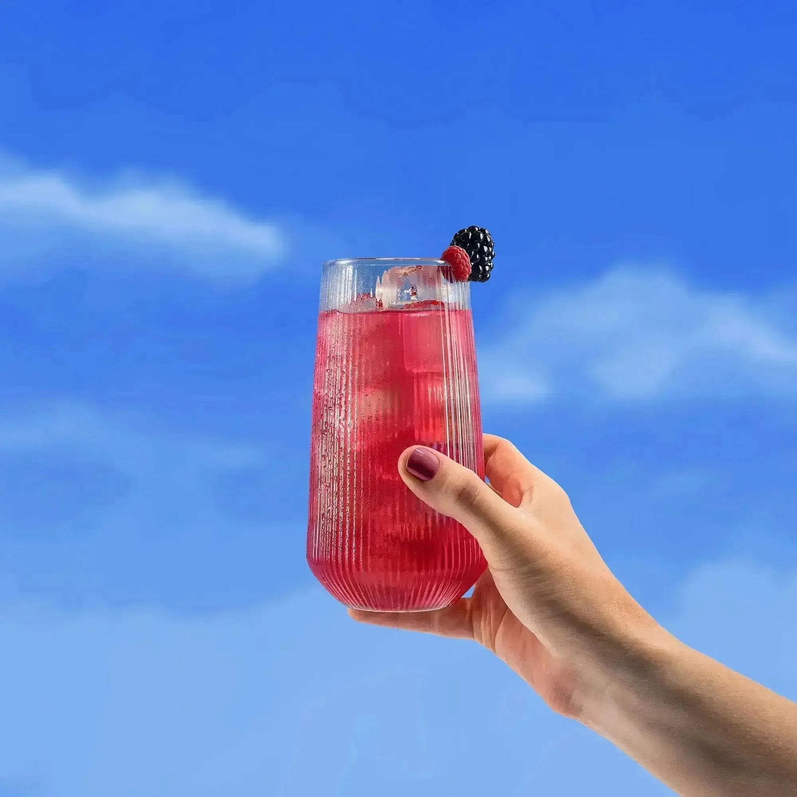 Hand holding a pink Spacegoods Glow Dust berry drink against a blue sky