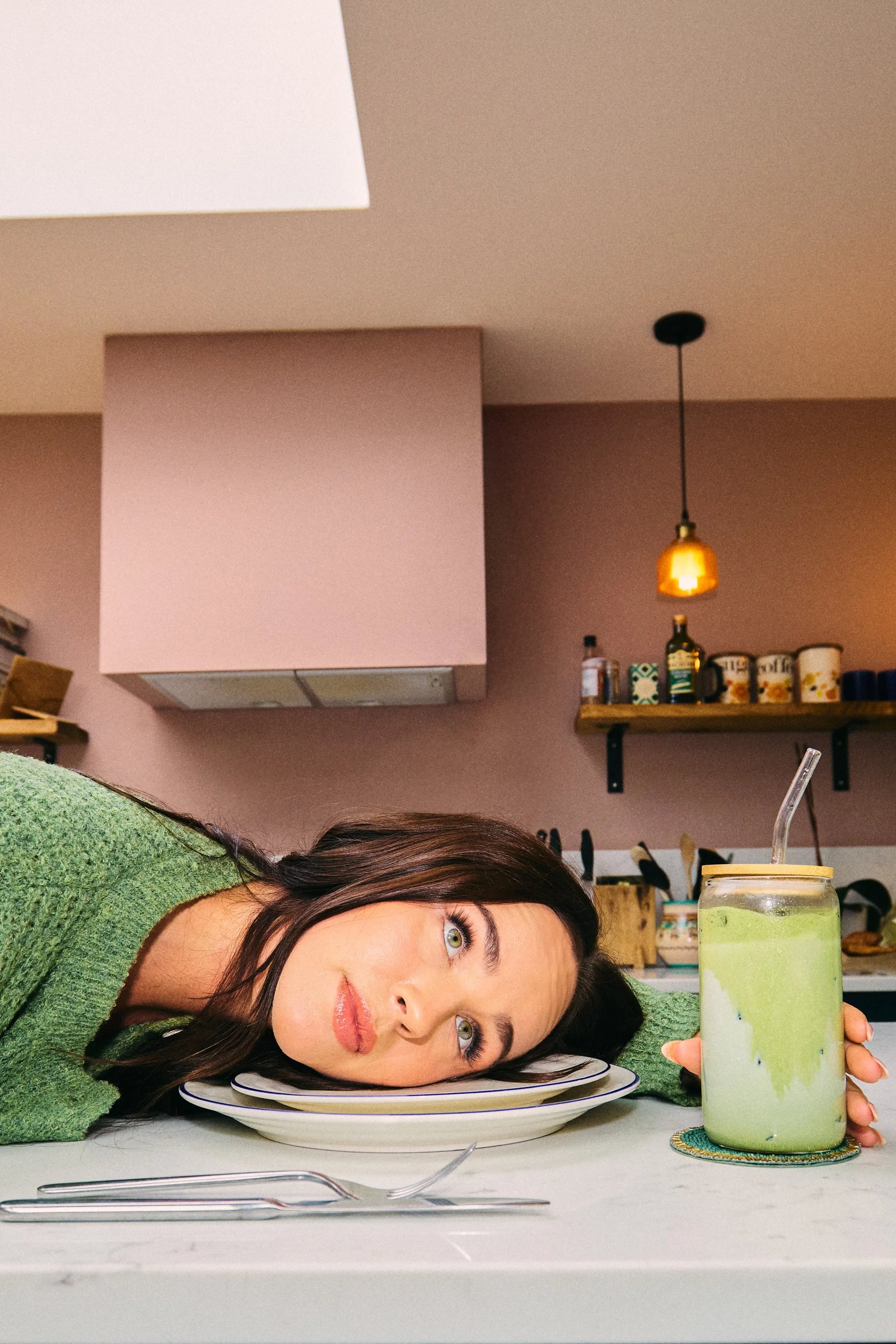 Woman resting her head on a kitchen counter beside an iced matcha drink