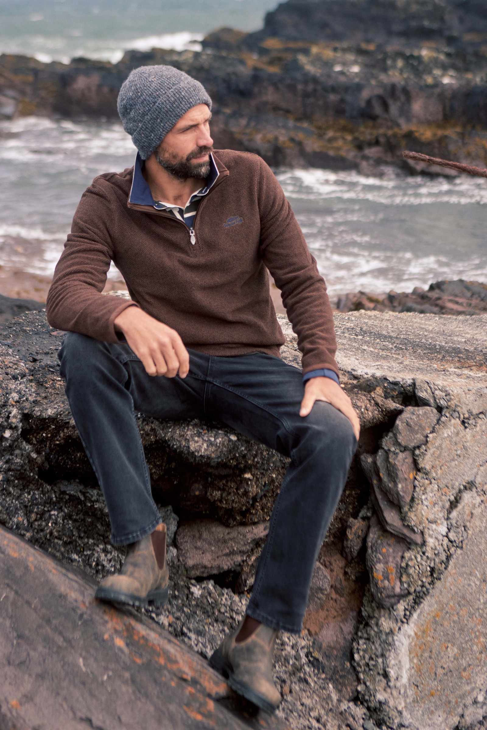 Man in the Weird Fish Errill quarter zip textured fleece sitting on coastal rocks
